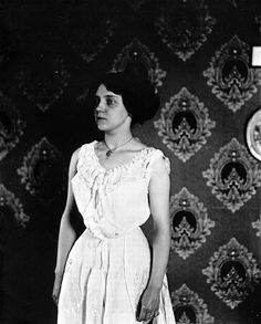 an old black and white photo of a woman standing in front of a wallpapered background