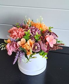 a white vase filled with lots of colorful flowers on top of a black table next to a wall