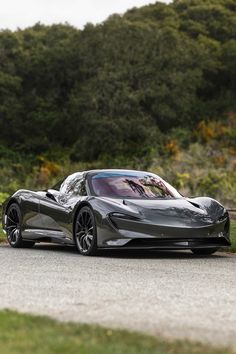 a silver sports car driving down a road next to some grass and trees in the background