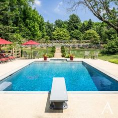 an empty swimming pool surrounded by lawn chairs and umbrellas with trees in the background