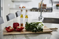 two bottles of olive oil sit on a cutting board next to peppers and lettuce