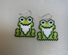 a pair of green and white beaded earrings with a smiling frog on it's face