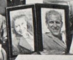 an old black and white photo of two people in front of a table with pictures on it