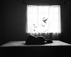 black and white photograph of a person laying on a bed in front of a window