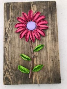 a pink flower with green leaves is on a wooden board and has a purple circle in the center