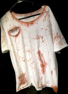 a white t - shirt with red stains on it hanging from a clothes rack in the dark