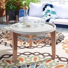 a coffee table with glasses on it in front of a couch and potted plant