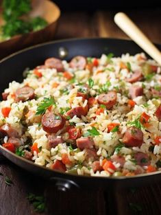 a skillet filled with rice and sausages on top of a wooden table next to parsley