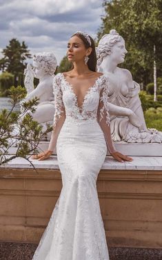 a woman standing in front of a statue wearing a wedding dress with long sleeves and an open back