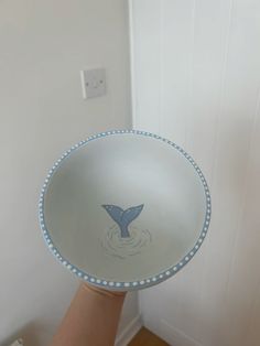 a hand holding a blue and white bowl with a whale design on it's side