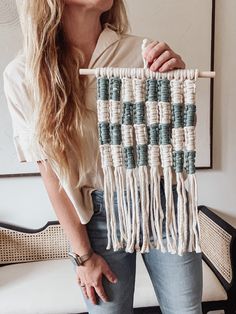 a woman is holding an art piece made out of macrame beads and yarn