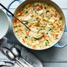 a pot filled with chicken noodle soup on top of a wooden table next to a spoon