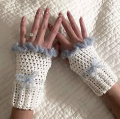 a woman's hands with crocheted gloves on top of a bed