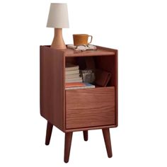 a nightstand with a lamp on top of it and books in the bottom drawer next to it