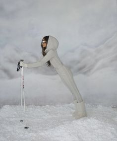 a woman in white ski suit standing on top of snow covered ground with ski poles