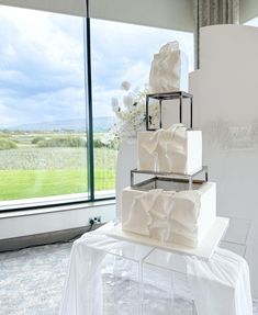 a three tiered white cake sitting on top of a table next to a window