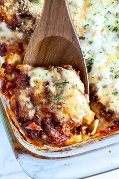 a wooden spoon in a casserole dish with meat and cheese on the side