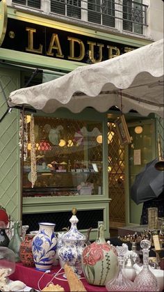 there are many vases on the table in front of the storefront and under an umbrella