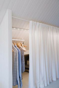 an open closet with clothes hanging on hangers and white drapes covering the walls