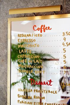 the menu for coffee is written in gold on a glass board with writing and numbers