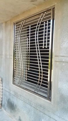 a window on the side of a building with metal bars in it and a cat sitting next to it