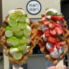 two waffles topped with fruit and whipped cream are being held up in front of a building