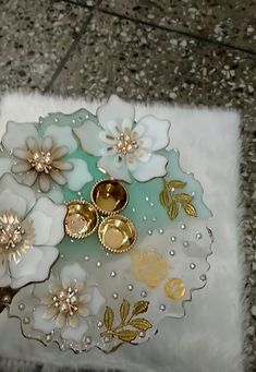 a white and gold plate sitting on top of a floor next to a flower arrangement