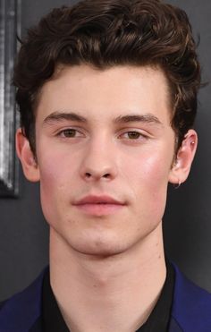 a close up of a person wearing a blue suit and black shirt with his hair pulled back