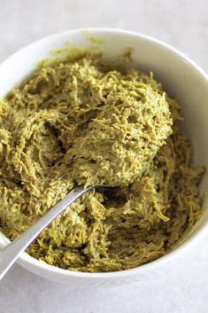 a white bowl filled with green food on top of a table next to a spoon