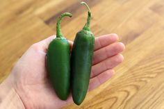 two green peppers sitting in the palm of someone's hand