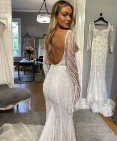 a woman in a wedding dress looking back at the camera while standing in front of a mirror