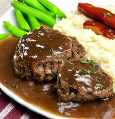 a white plate topped with meat and gravy next to green beans