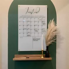 a calendar is on the wall next to a vase with some dry grass in it