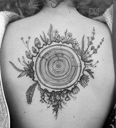 the back of a woman's shoulder with a tree stump and flowers on it