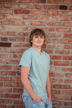 a young man standing in front of a brick wall with his hands in his pockets