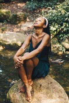 a woman sitting on top of a rock next to a river