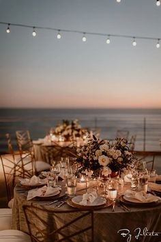 a table set up with candles and flowers on it for an outdoor dinner by the ocean