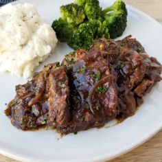 a white plate topped with meat and broccoli covered in gravy next to mashed potatoes