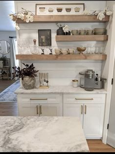 a kitchen with white cabinets and marble counter tops, gold accents on the shelves above