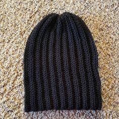 a black knitted hat laying on top of a brown carpet next to a pair of scissors