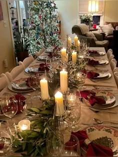 a dining room table set for christmas dinner with candles and place settings on the table