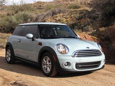 a small white car driving down a dirt road