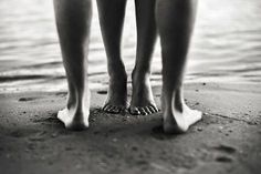 two people standing next to each other on the beach with their feet in the sand