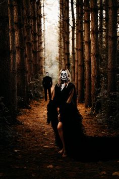 two people dressed in black and white are walking through the woods with their faces painted