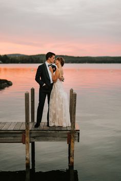 a bride and groom standing on a dock at sunset