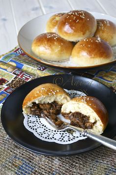 two plates filled with sandwiches on top of a table next to another plate full of buns