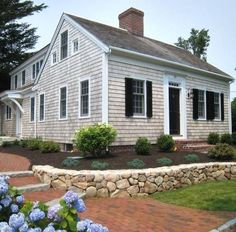 a white house with black shutters and blue hydrangeas