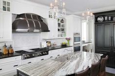 a large kitchen with marble counter tops and white cabinetry, along with black appliances