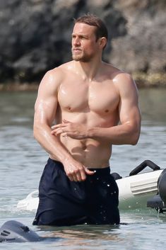 a shirtless man standing in the water with his surfboard