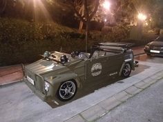 an army green car is parked on the side of the road at night with its hood up